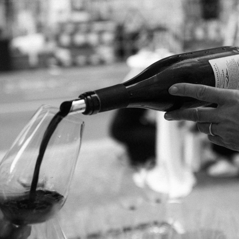 Wein in der Gastronomie Ein Glas wird mit Rotwein aus einer Flasche gefüllt.